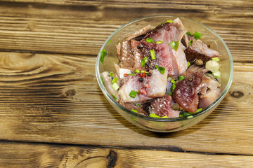 Delicious salted herring with spices in glass bowl on wooden table
