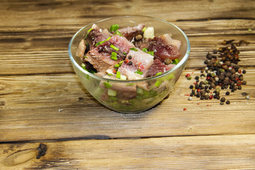 Delicious salted herring with spices in glass bowl on wooden table