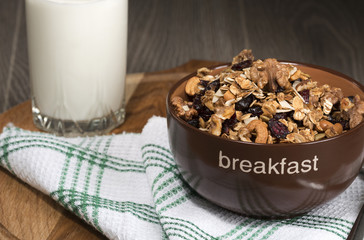Homemade granola with honey, oatmeal, cashew nut, almond, pistachio, raisin and cranberry in clay bowl,glass with milk on wood dark table,