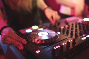 Obraz premium Hands of woman DJ tweak various track controls on dj's deck at night club 