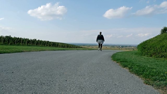 Young woman walking on empty countryside road near vineyards on sunny day
