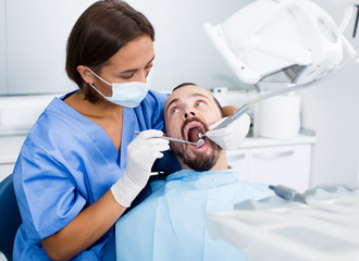 Dentist female in uniform is examinating of male in dental clinic