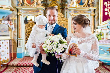 Happy wedding couple in the church with their little baby daughter on their wedding day.