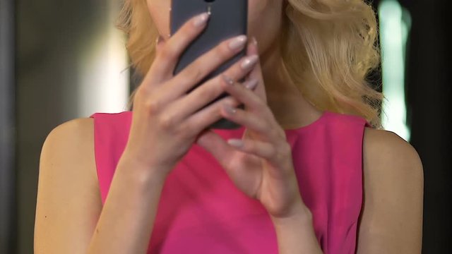 Blond female looking at reflection in mobile phone screen, preparing for date