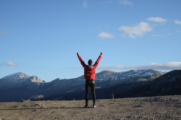 Back view of successful sporty man celebrating training goals towards and freedom on the mountain and sky in late winter.