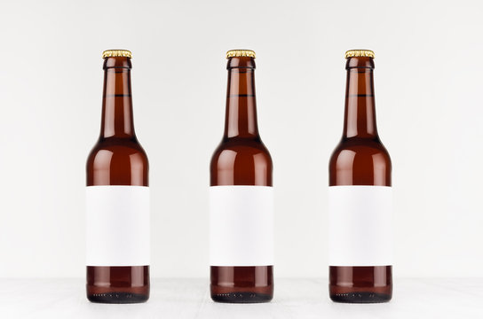 Three brown longneck beer bottles 330ml with blank white label on white wooden board, mock up. Template for advertising, design, branding identity.