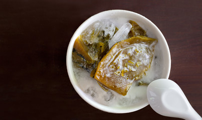 Pumpkin in syrup with coconut milk and ice, Thai sweet dessert in white bowl on dark wooden table