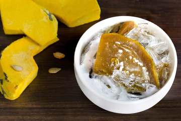 Pumpkin in syrup with coconut milk and ice, Thai sweet dessert in white bowl on dark wooden table