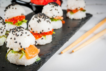 Trend hybrid food. Japanese Asian cuisine. Mini sushi-burgers, sandwiches with salmon, hayashi wakame, daikon, ginger, red caviar. White marble table, with chopsticks, soy sauce. Copy space