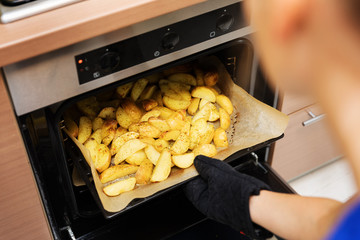 woman removing prepared potatoes tray out of oven