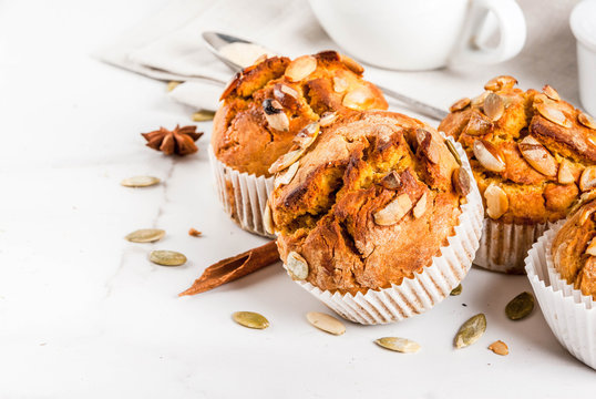 Autumn and winter baked pastries. Healthy pumpkin muffins with traditional fall spices, pumpkin seeds. With tea cup. White marble table, copy space