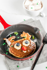 Funny food for Christmas. Kids breakfast pancake decorated like reindeer, with hot chocolate with marshmallow, white table copy space top view