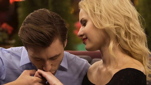Handsome man kissing hand of blond woman, putting heads together, escort girl
