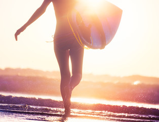 Woman with surfboard runs into the ocean during sunset