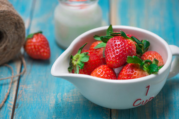 Bowl with fresh strawberry on blue wooden table.