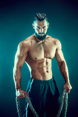 Muscular bearded bodybuilder man Posing with ropein studio.