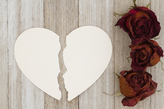 Dead red roses with torn heart-shape card on weathered wood background