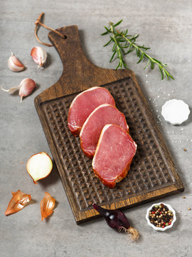 Raw fresh slices meat on a rustic wooden cutting board with rosemary and spices. Selective focus.
