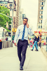 Young African American Businessman traveling, working in New York, wearing white shirt, tie, black pants, leather shoes, carrying laptop computer, talking on cell phone, walking on street in Manhattan