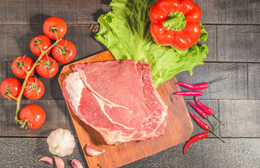A raw piece of beef with peppers, tomatoes, herbs and garlic