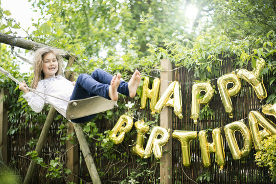 Portrait of swinging girl in garden with decoration for Birthday Party in the background