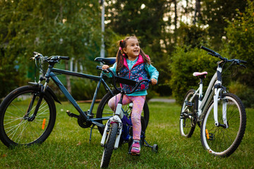 Obraz premium Little girl riding a bicycle in the park on the road covered with autumn oak and maple trees
