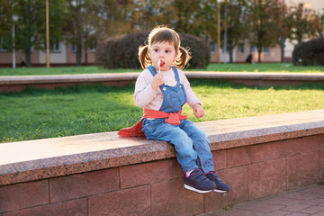 Cute beautiful child eats candy.little girl in denim jumpsuit.