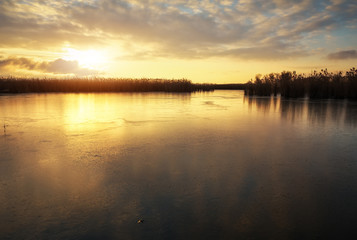 Fototapeta na wymiar Winter landscape with frozen river and sunset sky. Composition of nature.