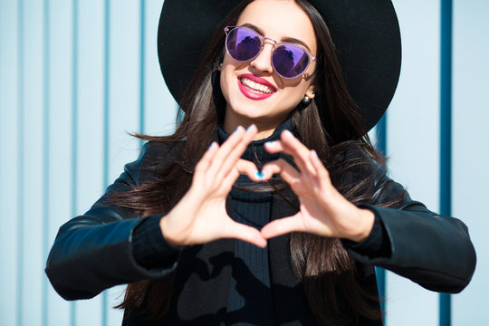 Happy young woman in glasses making a heart shape with her hands