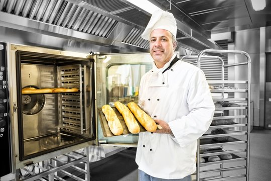 Proud mature baker showing three baguettes