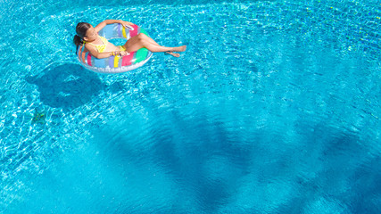 Aerial view of girl in swimming pool from above, kid swim on inflatable ring donut and has fun in water on family vacation
