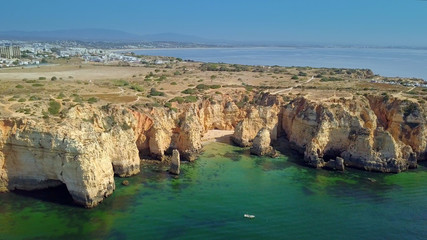 Fototapeta na wymiar Aerial shot taken with drone of panoramic view with rocky cliffs of coastline and city placed above on hills and shoreline, Portugal, Algarve.
