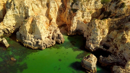 Fototapeta na wymiar Aerial shot of colorful landscape with white rough cliffs of tropical ocean coastline and green water of calm lagoon, Portugal, Algarve.