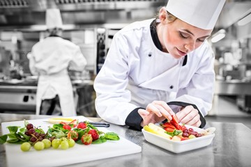Female chef putting a strawberry in the fruit salad