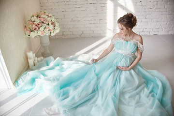 Pregnancy, woman sitting on the floor in a Deluxe dress and holding hands over her belly. The woman awaits the birth of a baby. Loving wife