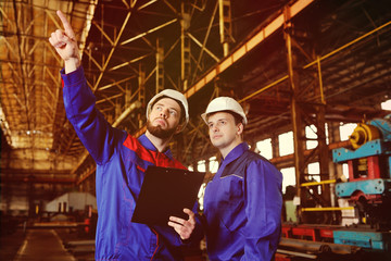 Obraz na płótnie Canvas Engineer-constructor and worker discuss the construction project against the background of an industrial plant