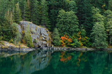 Autumn colors by a peaceful lake with a large rock formation and forest background.