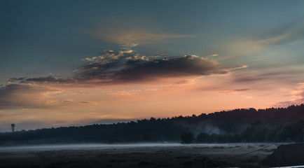 A beautiful red sunset with blue sky and white fog on the field
