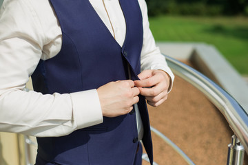Young handsome man buttoning vest of blue suit. Getting ready for formal event concept. Horizontal...