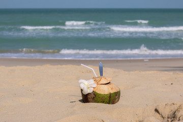 Coconut with drinking  straw, spoon  and beautiful white Plumeria flower on the white sand beach in Nakhonsrithammarat province ,Thailand. Blue sea blur background.
