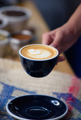 Perfectly brewed cappuccino and fresh roasted Arabica beans in the cozy atmosphere of a coffee shop. Professional barista or a client is going to taste a cup of coffee.