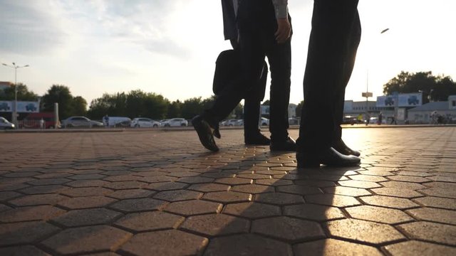 Feet of three businessmen walking in city with sun flare at background. Business men commute to work together. Confident guys being on his way to office. Colleagues going outdoor. Slow motion Close up