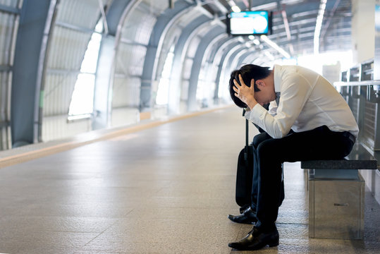 Train Delay Or Problem In The Train Station, Tired Desperate Aisan Passenger Waiting In The Terminal With Suitcase..