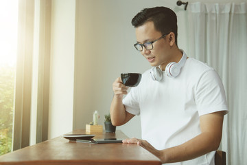 Young asian man drinking coffee and using digital tablet in coffee shop.