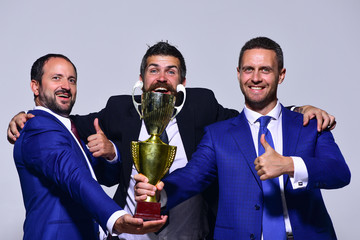 Company leaders hold golden prize, show thumbs up and hug