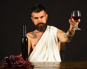 Man with beard holds glass of wine on brown background.