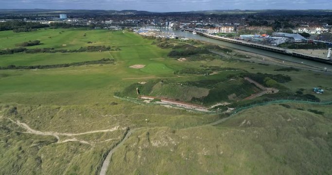 Aerial pull out view from a links golf course by a village on the mouth of a river in Southern England