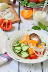 Vegetarian healthy salad with fresh ripe summer vegetables: tomato, cucumber,  pepper and onion on light wooden background