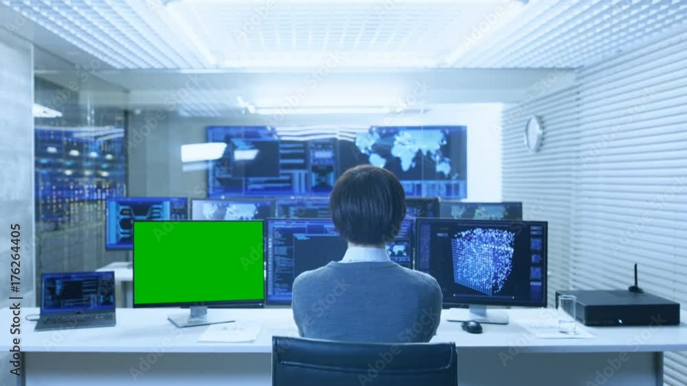Poster Back View of the IT Technician Working on with Neural Network on His Personal Computer with Green Screen Mock-up. He Works in a Big System Control Data Center with Multiple Monitors Showing Graphics.