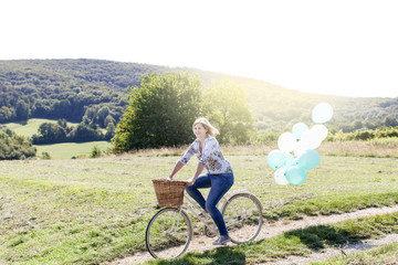 Happy Woman driving by bike with balloons